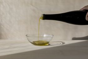 pouring olive oil from a darlk glass bottle into a glass bowl 