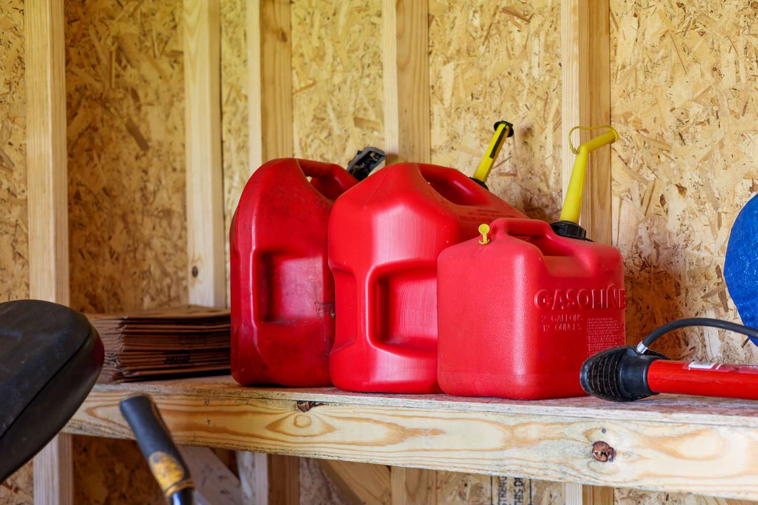 Red plastic gas containers on a wooden shelf in a storage area
