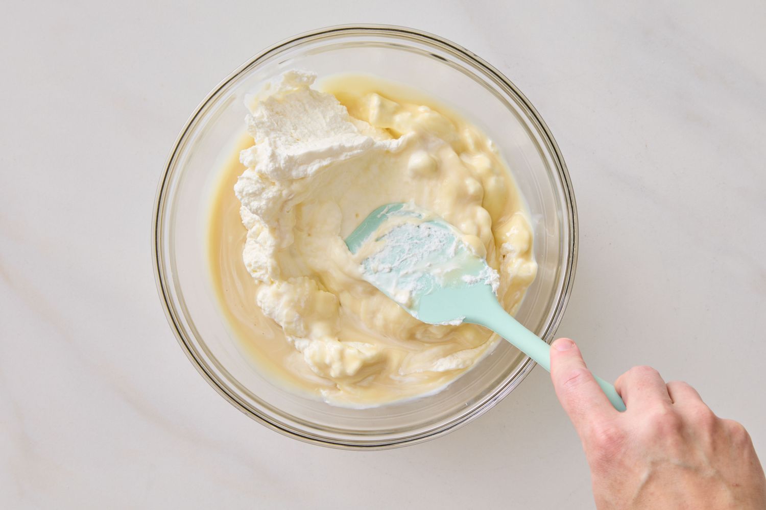 A person mixing ingredients in a glass bowl with a spatula