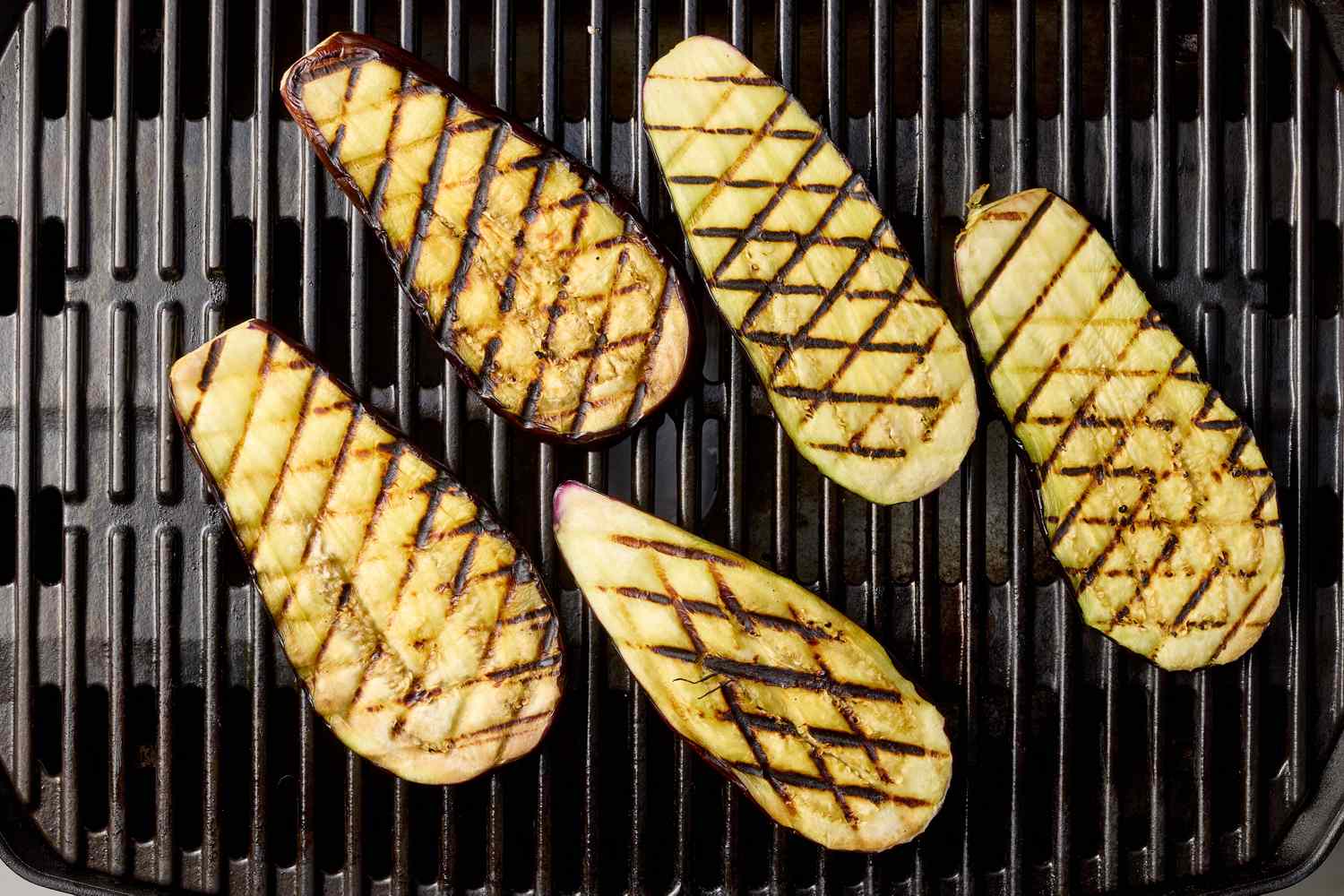 Slices of eggplant with grill marks on a grate, arranged in a neat pattern