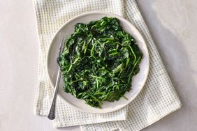 A plate of steamed spinach with a fork resting on the side placed on a patterned cloth