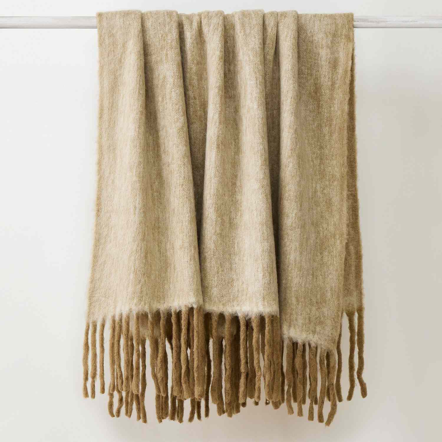 A fiber throw blanket with long fringe draped over a rod