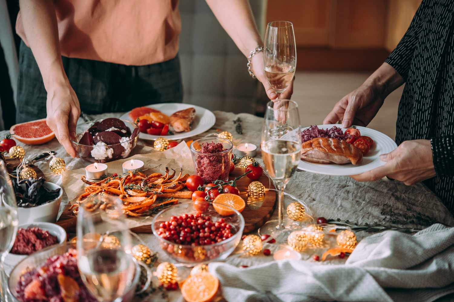 A festive table setup with food candlelights and two people holding plates and glasses of champagne