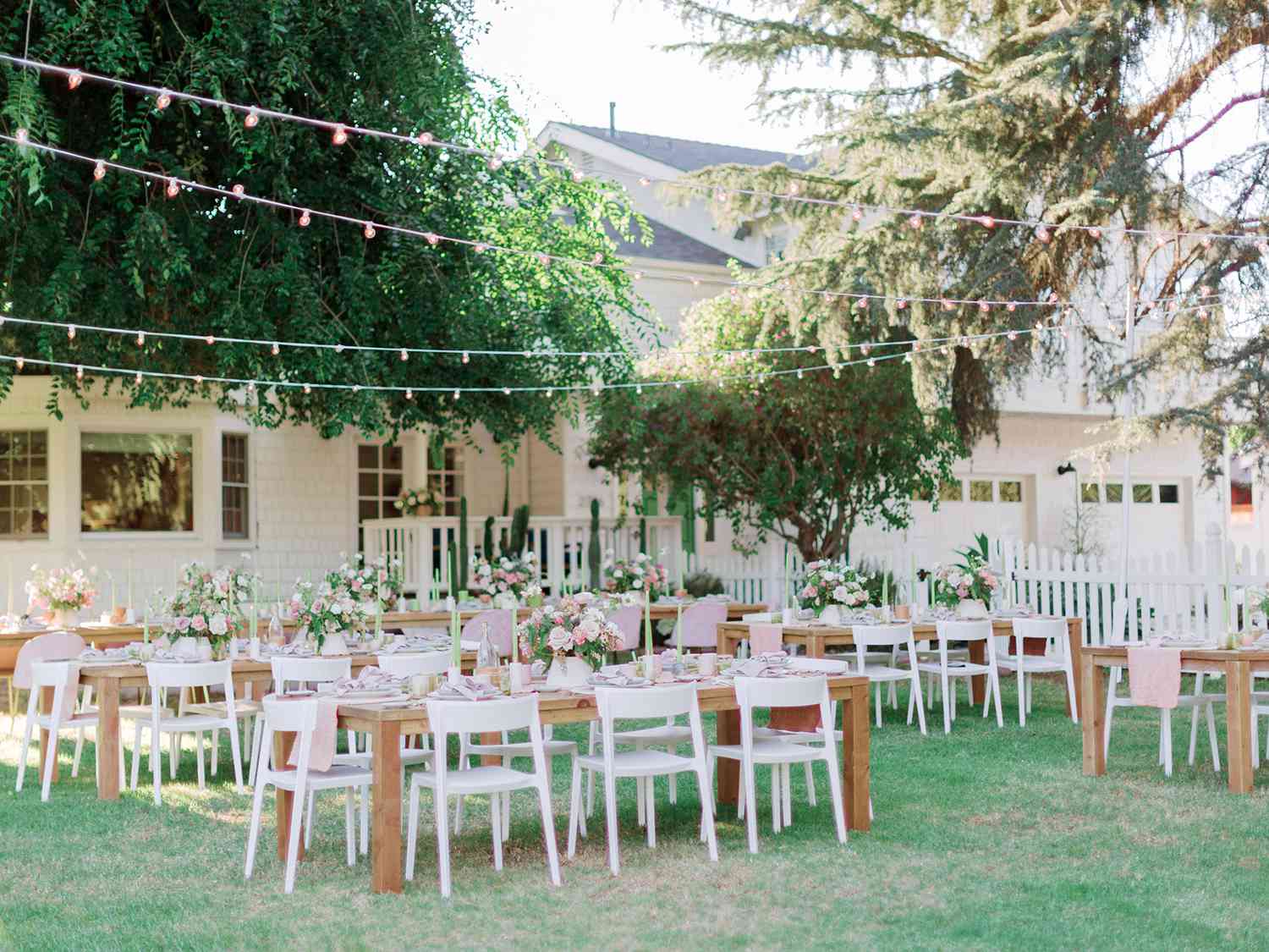 long wooden tables outdoors with white chairs and overhead string lights