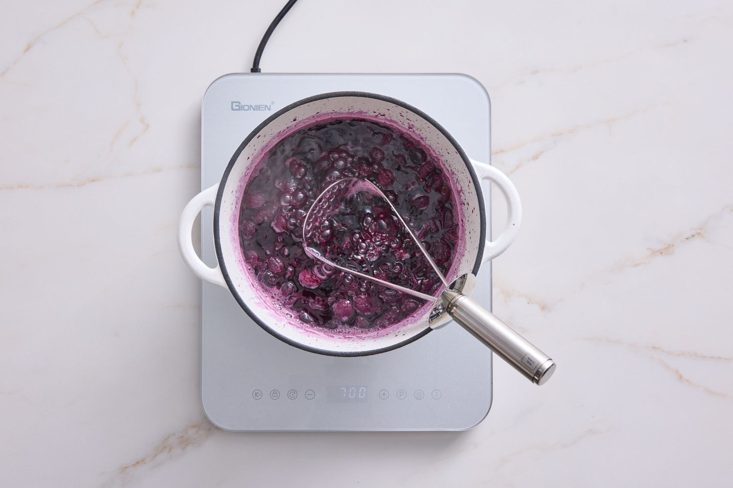 Cooking fruit mixture in a pot on an induction cooktop with a masher
