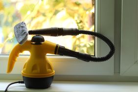A handheld steam cleaner with a nozzle and hose placed on a windowsill
