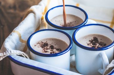 Three mugs of hot chocolate in enamel cups one being poured