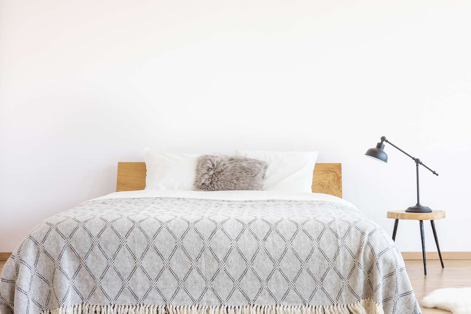 A neatly arranged bed with a patterned blanket a fur pillow and a small side table with a lamp