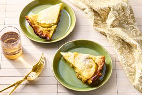 Two servings of Dutch baby pancake on green plates with utensils and fabric napkin