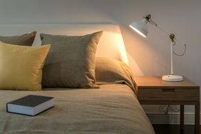 A bed with pillows a wooden nightstand a lamp and a book