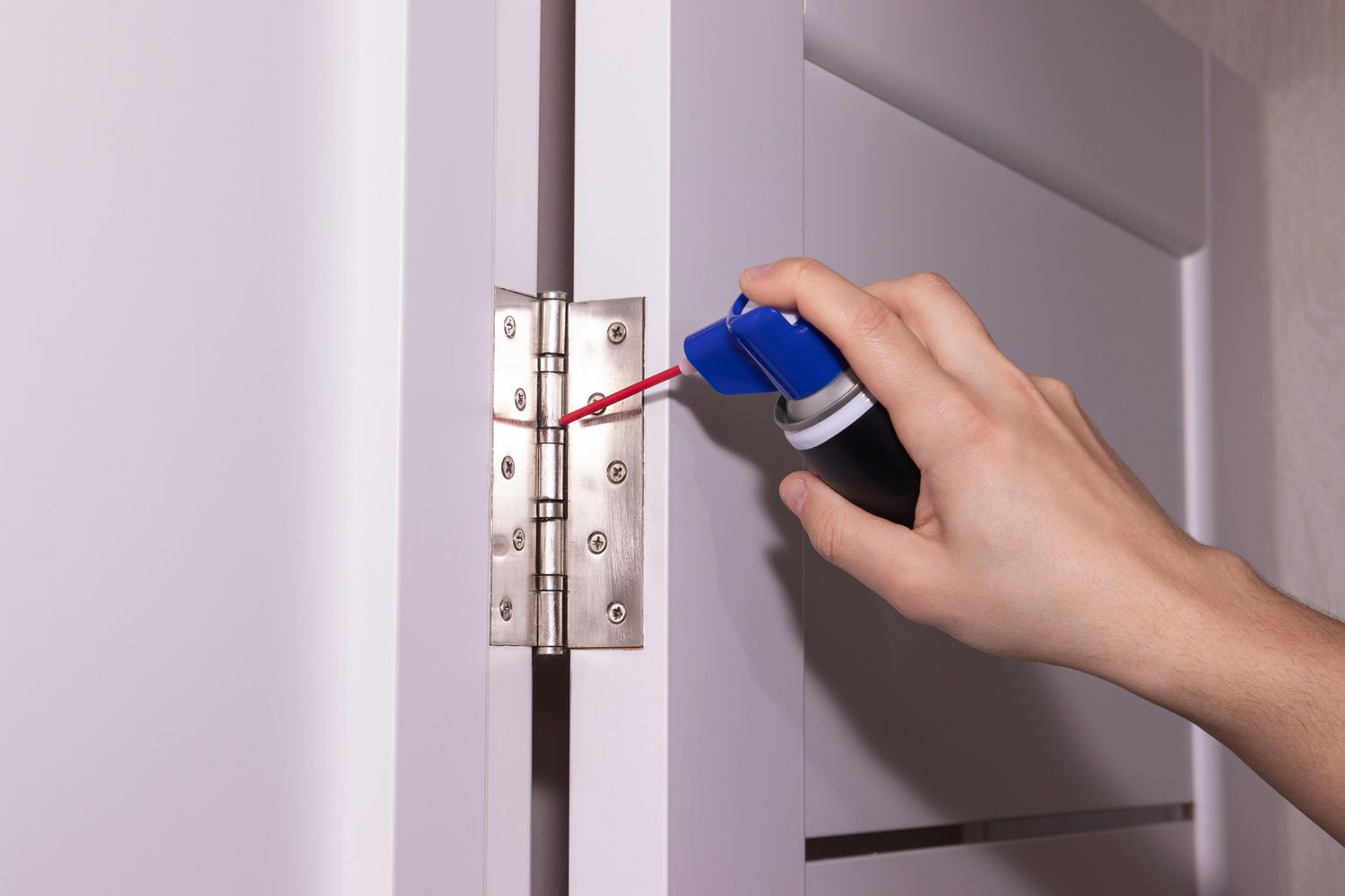 Hand applying lubricant to a door hinge
