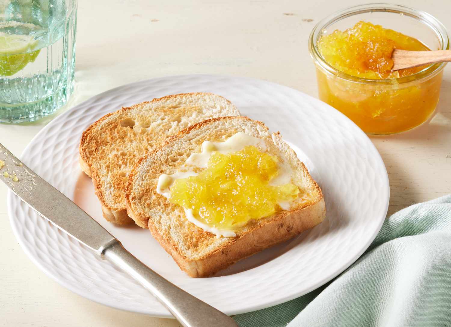 two pieces of toast with pineapple jam on it and glass container of jam