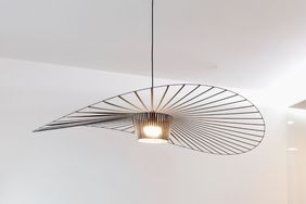 A modern ceiling light with a linear wave design suspended in a minimalist room