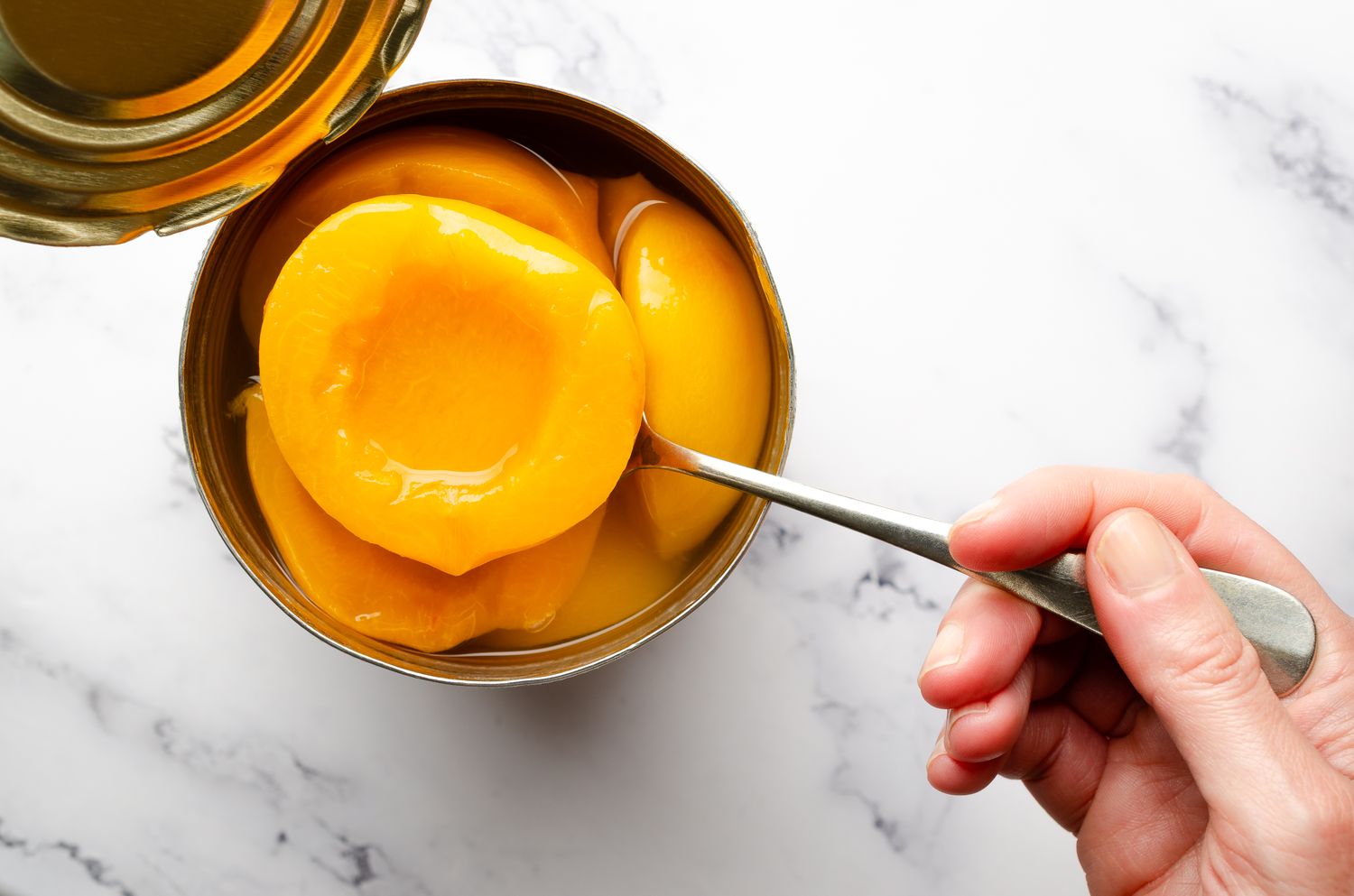 A spoon holding a half of a yellow peach preserved in a can