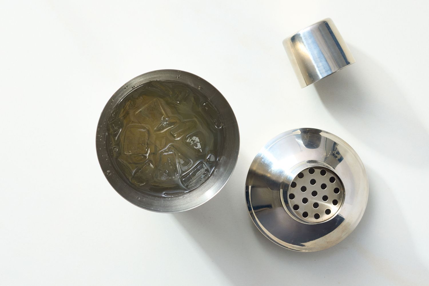 A metal cocktail shaker with its components containing a beverage with ice