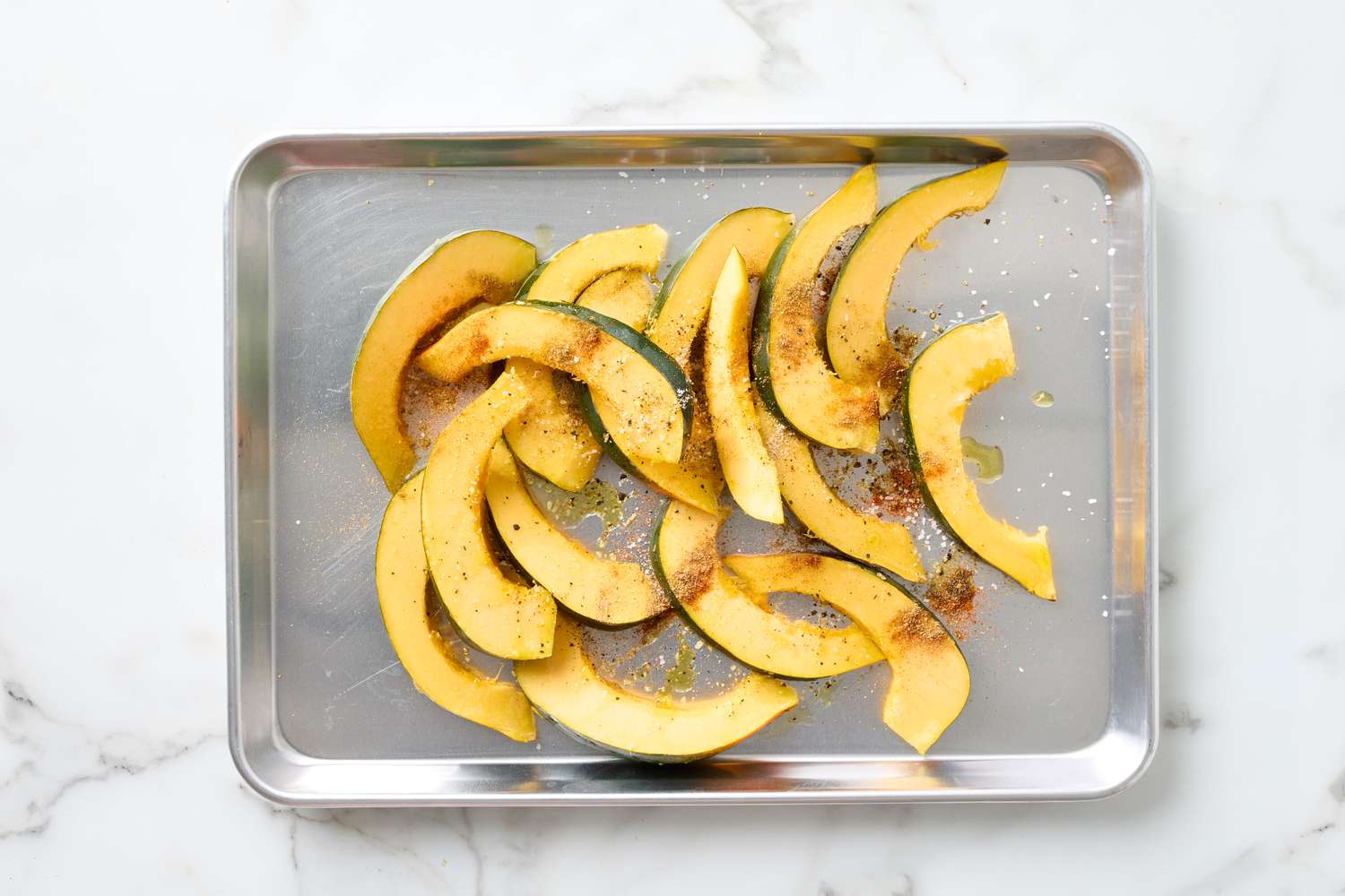 Sliced acorn squash seasoned on a baking tray