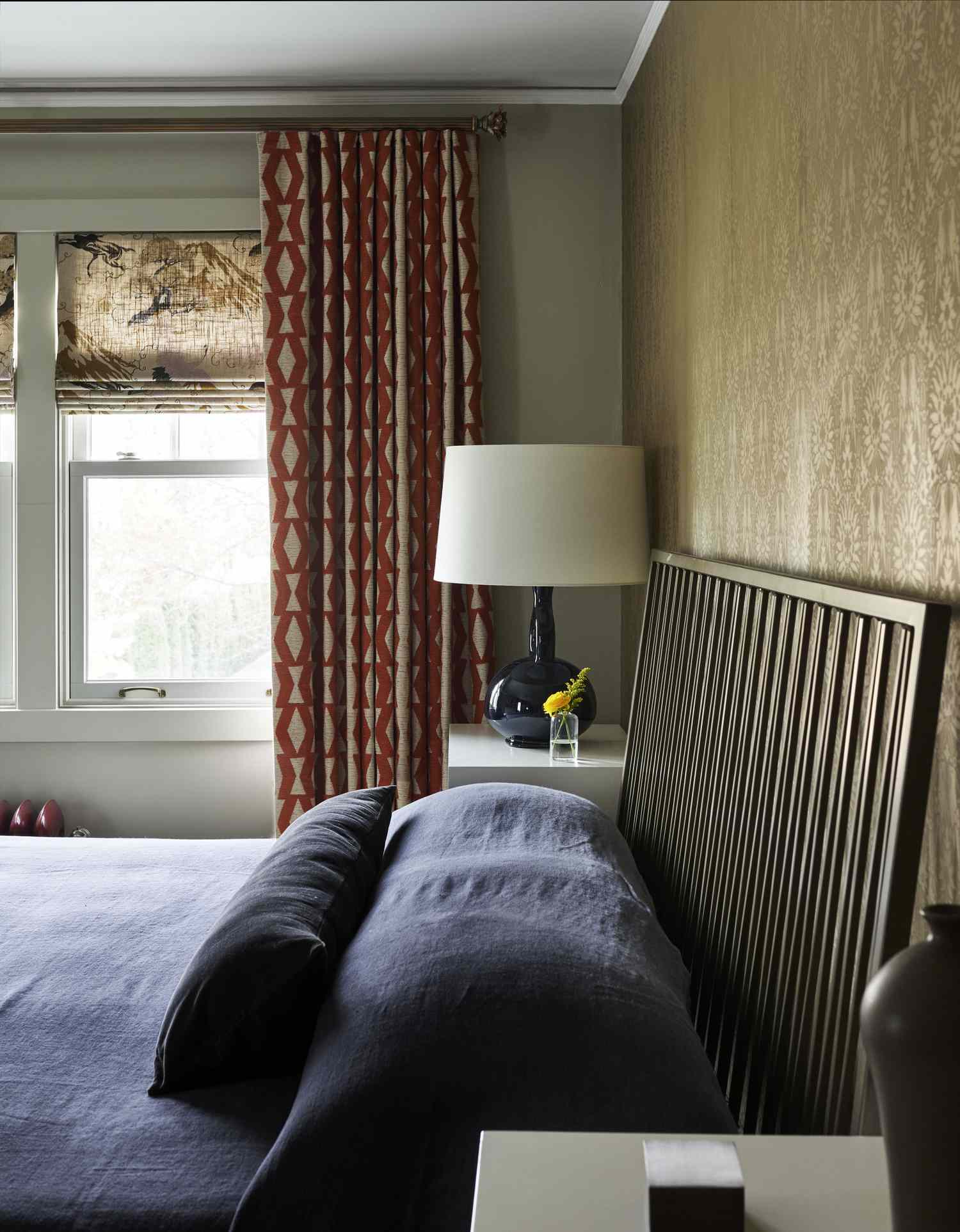 A bedroom with a window curtains a bed and a lamp on a side table