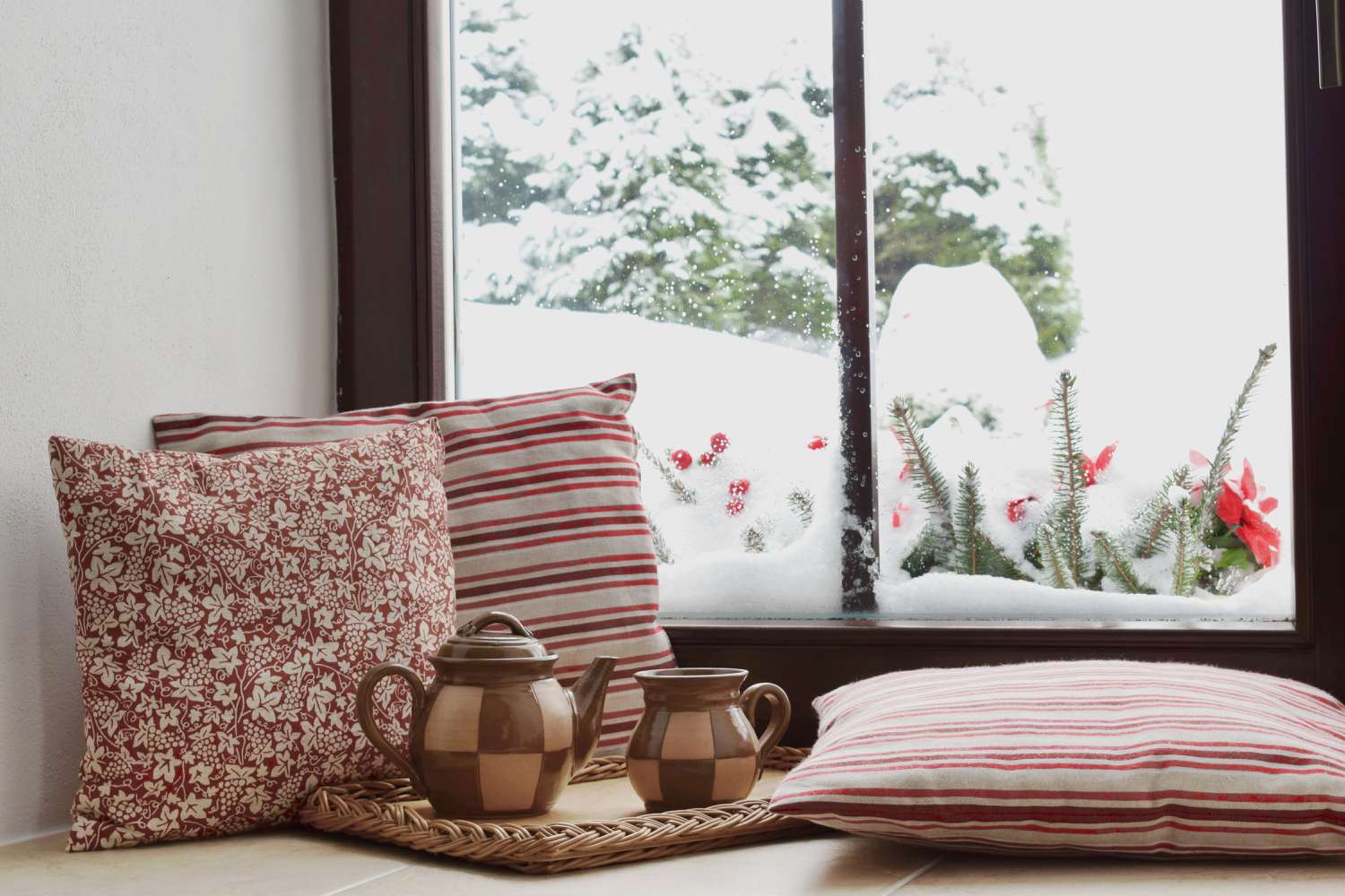 Tea set and pillows on window seat with snow outside