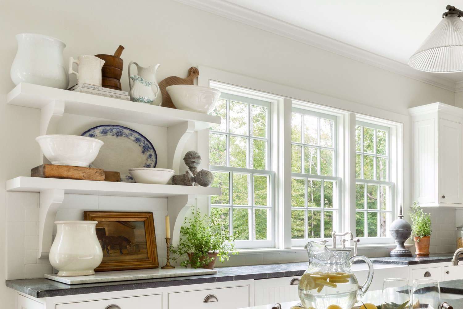 A kitchen scene featuring pottery and white shelves with a window overlooking greenery