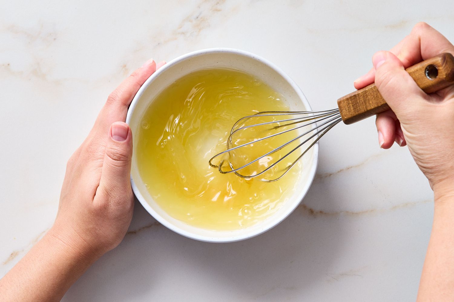 Mixing liquid in a white bowl using a whisk hands holding the bowl and whisk