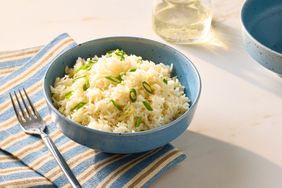 A bowl of rice garnished with green onions on a striped cloth alongside a fork