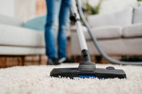 Person vacuuming a carpet in a living room setting