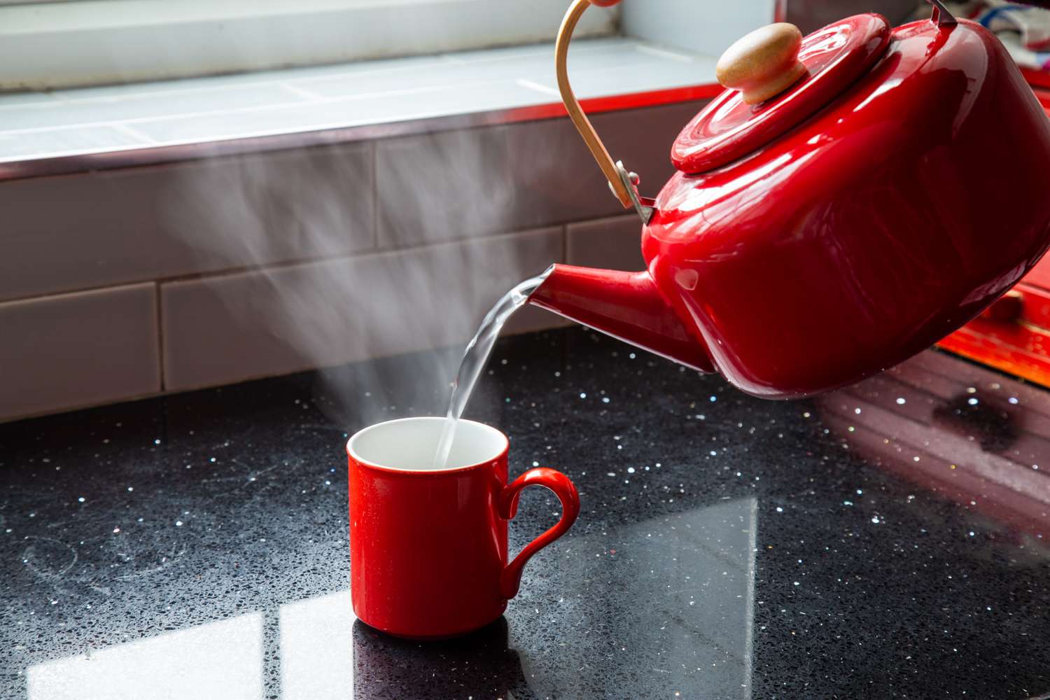 A kettle pouring hot water into a mug on a counter with steam rising from the cup