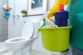 A person holding a bucket with cleaning supplies in a bathroom
