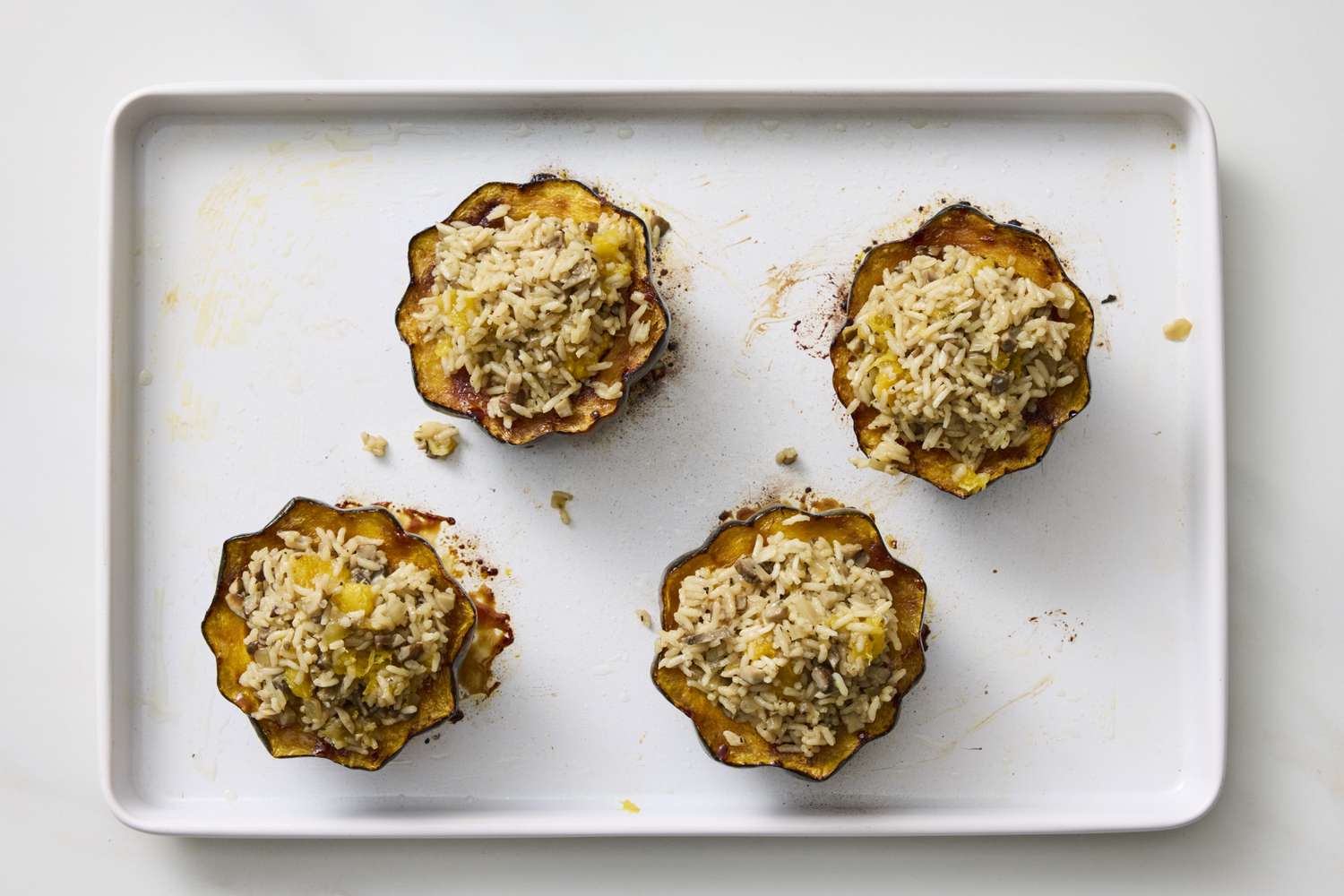 Four roasted acorn squash halves stuffed with a rice mixture on a baking sheet