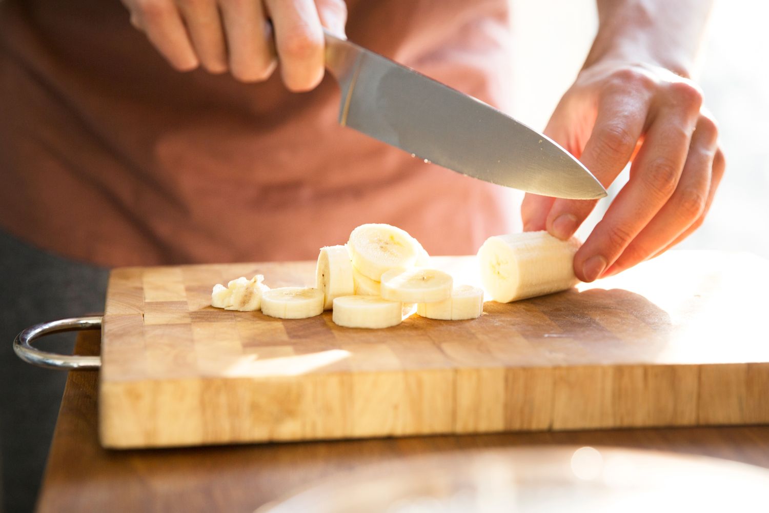 Someone cutting a banana on a wooden cutting board with a knife
