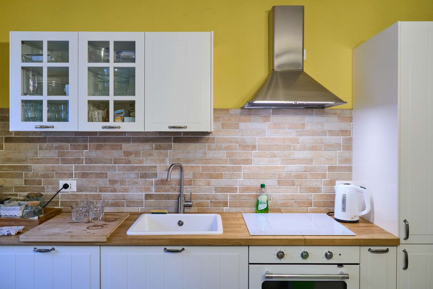 A modern kitchen with tiled backsplash a sink stovetop kettle and cabinetry