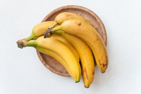Ripe yellow fruit bananas on wooden plate. White background. Healthy tropical food. Top view.
