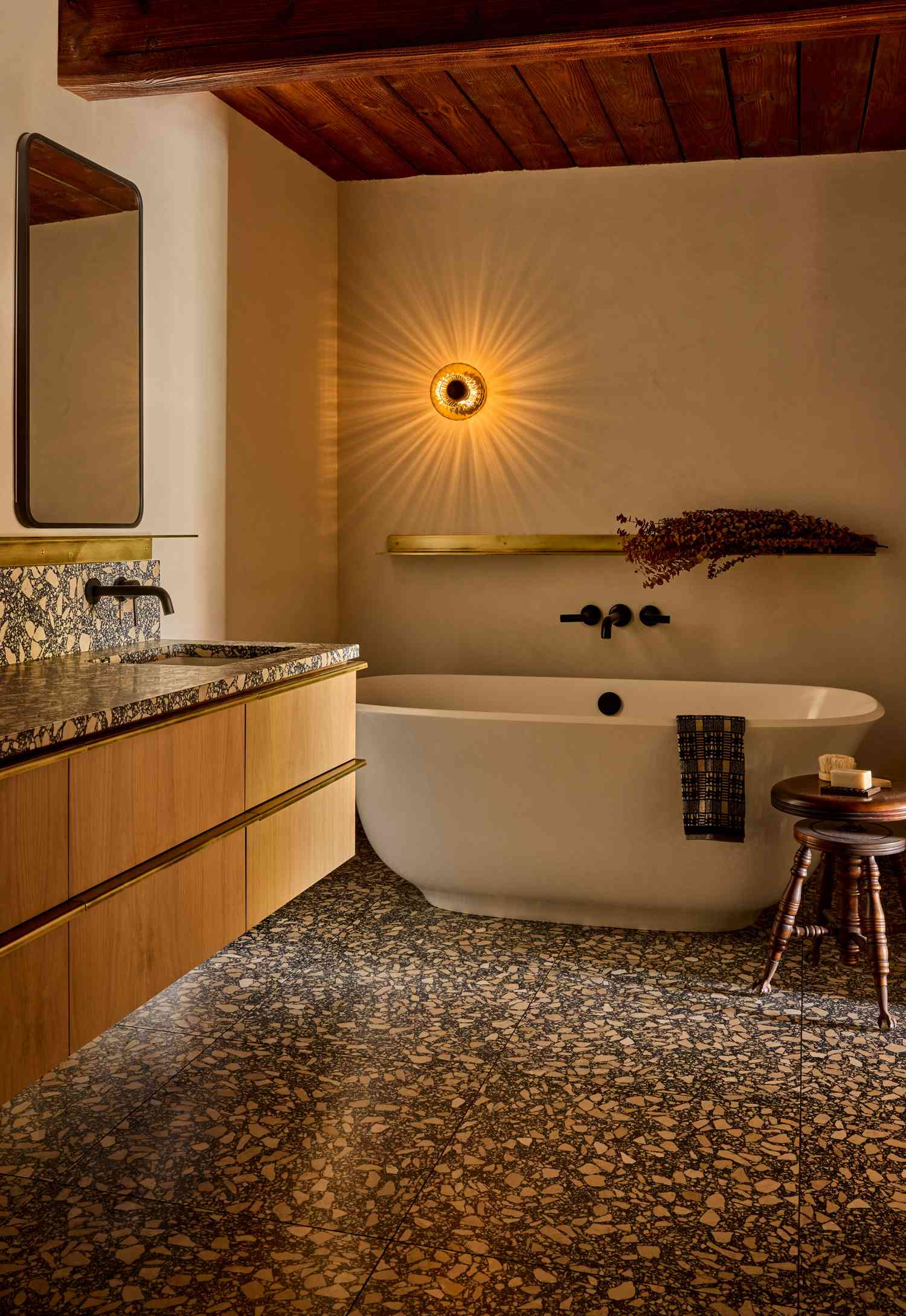A modern bathroom with a freestanding bathtub, wooden countertop, decorative wall fixture, and stone flooring